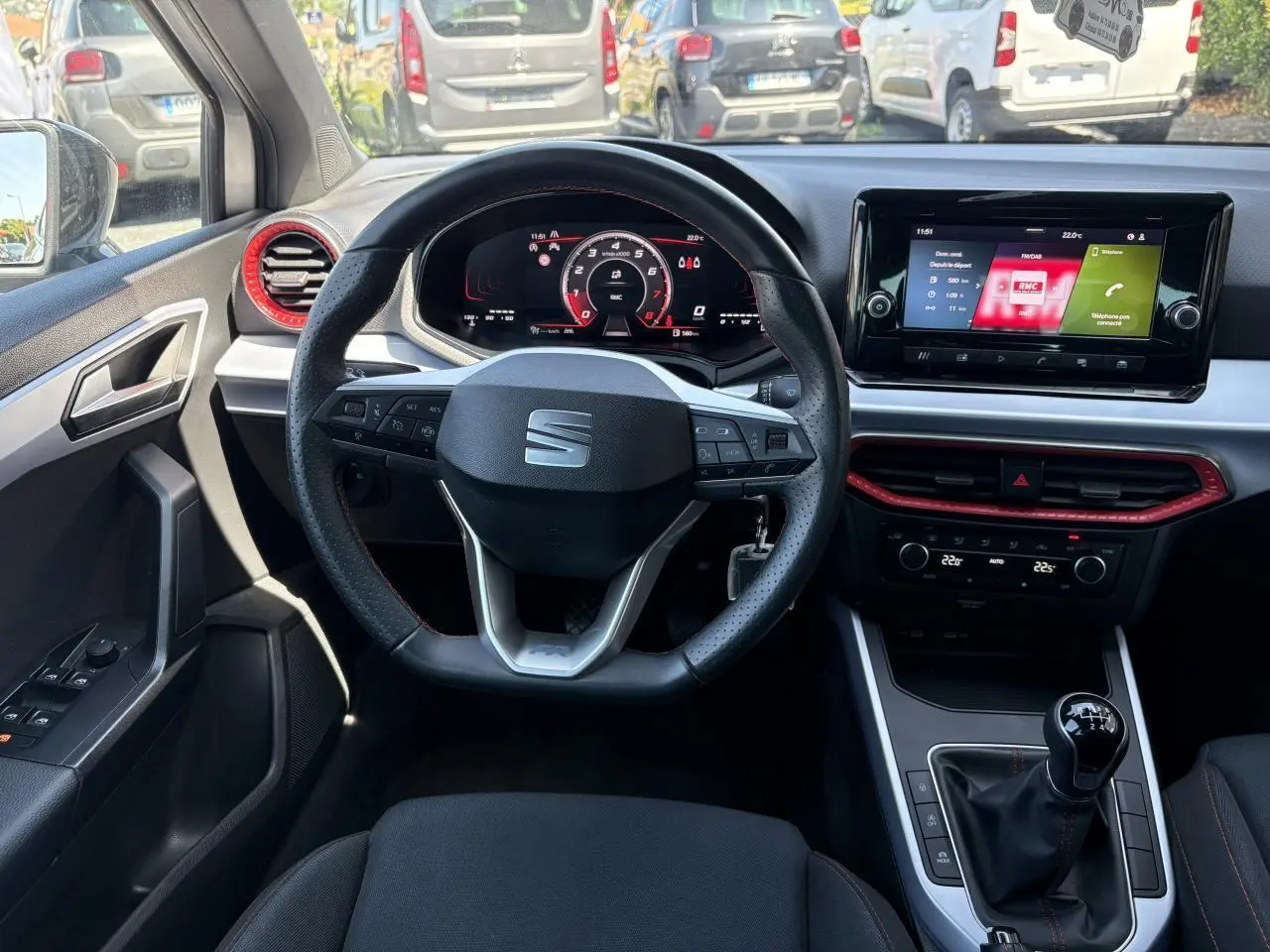 Intérieur SEAT Arona 2024 vu du siège conducteur, volant sport cuir, touches rouges autour des aérateurs et levier de vitesse manuel.