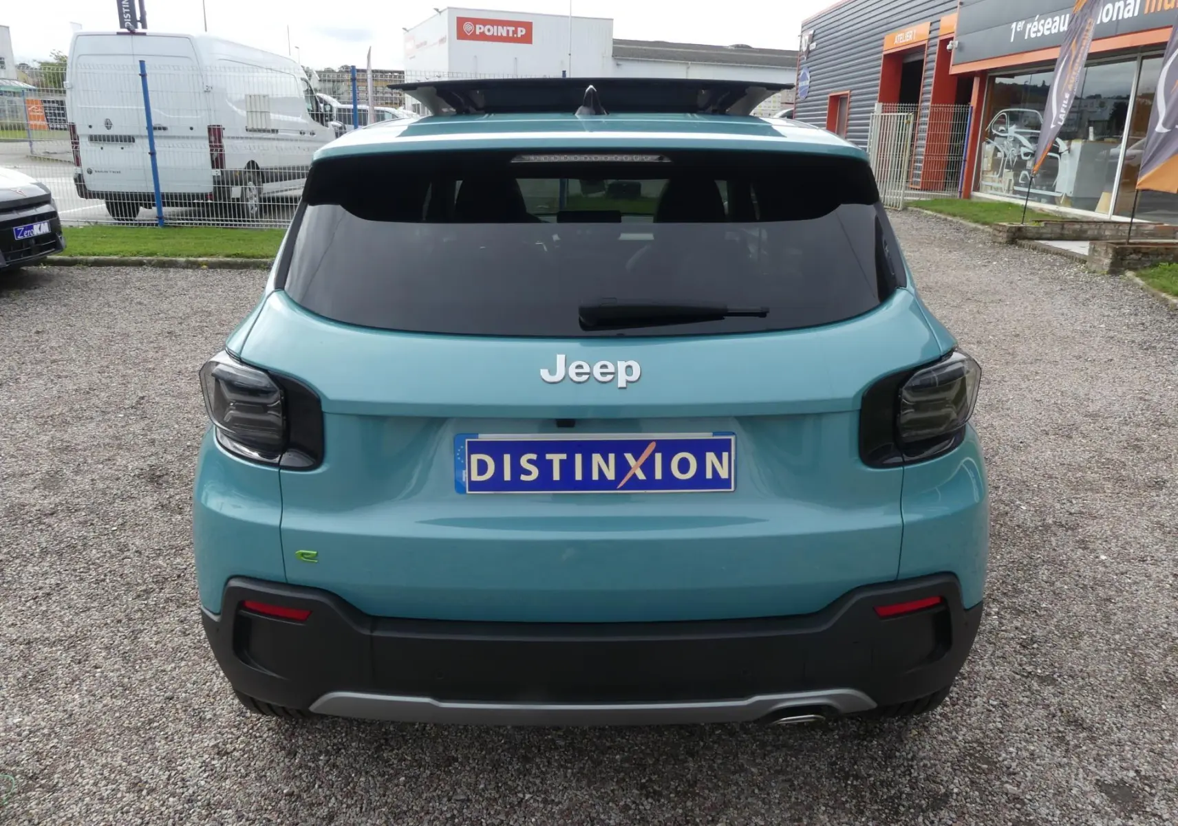 Vue arrière d'un Jeep Avenger bleu métallisé avec feux arrière fumés et plaque d'immatriculation Distinxion.