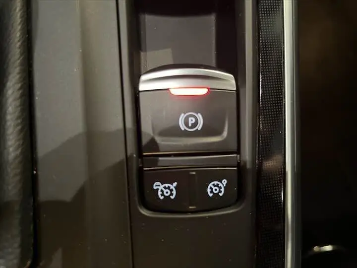 Gros plan sur les commandes électroniques du frein à main et régulateur de vitesse d'un Renault Scenic IV noir étoile métal.