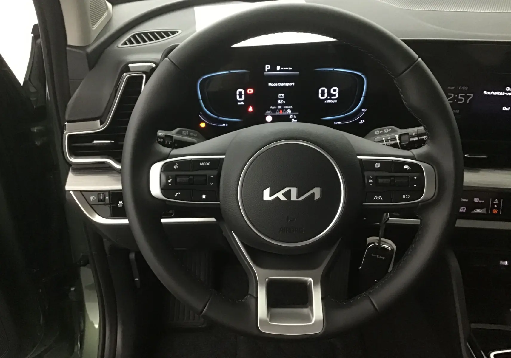 Vue rapprochée du volant noir du Kia Sportage 2025 vert Borneo, avec tableau de bord digital et commandes intégrées.