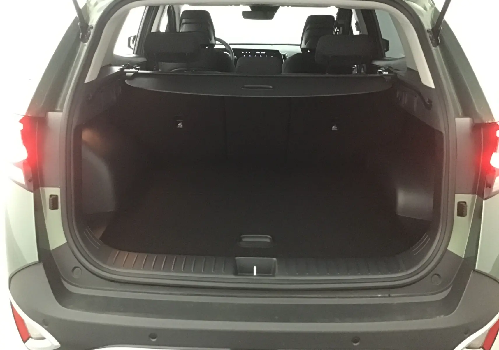 Coffre ouvert vu de l'arrière d'un KIA Sportage 2025 vert Borneo avec intérieur noir et feux arrière allumés.