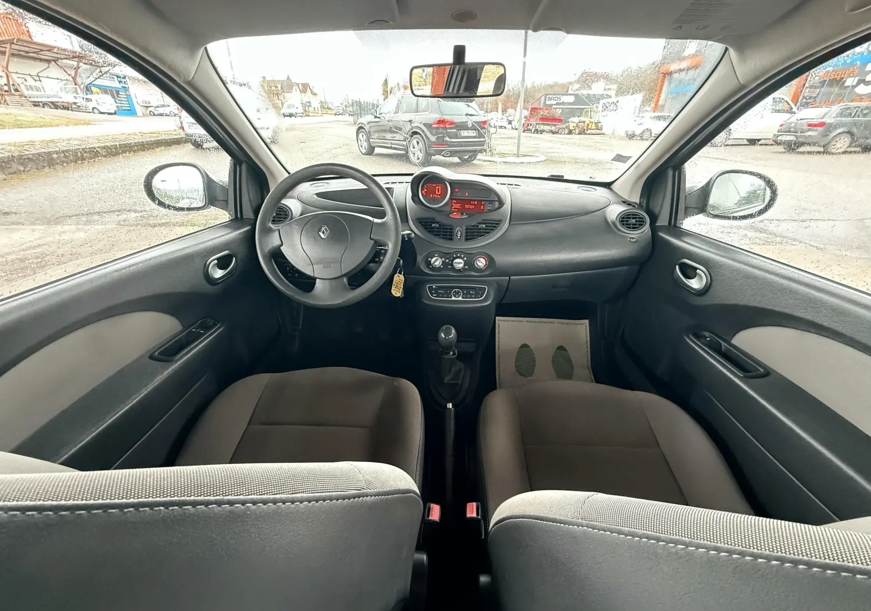 Vue intérieure avant de la Renault Twingo II gris, montrant le tableau de bord, volant et sièges en tissu gris.
