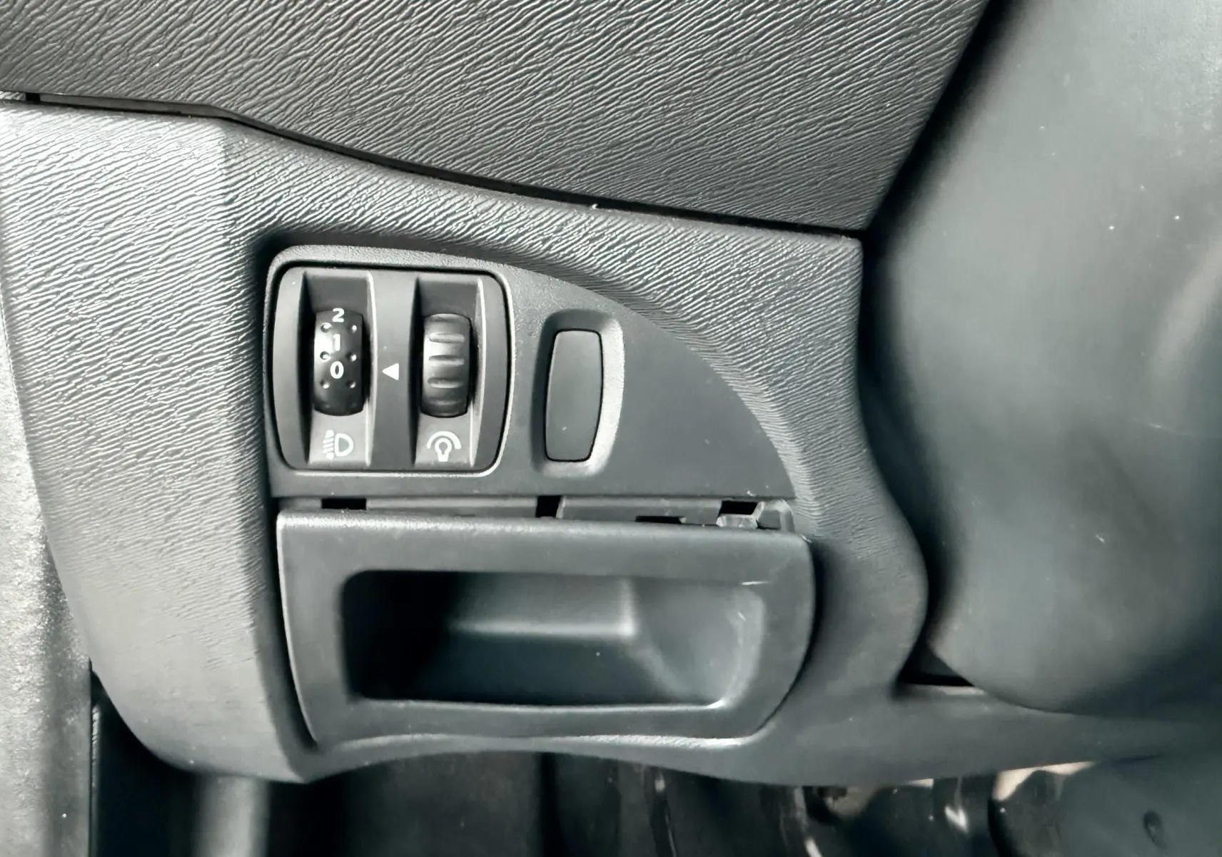 Gros plan sur les commandes d’éclairage et réglage du tableau de bord côté gauche d’une Renault Twingo II grise.