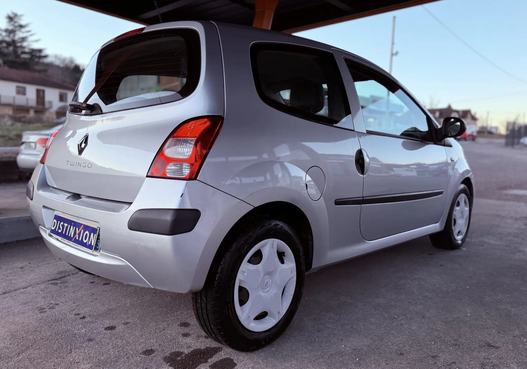 Vue 3/4 arrière droite d’une Renault Twingo II grise de 2009 avec jantes pleines blanches et hayon fermé.