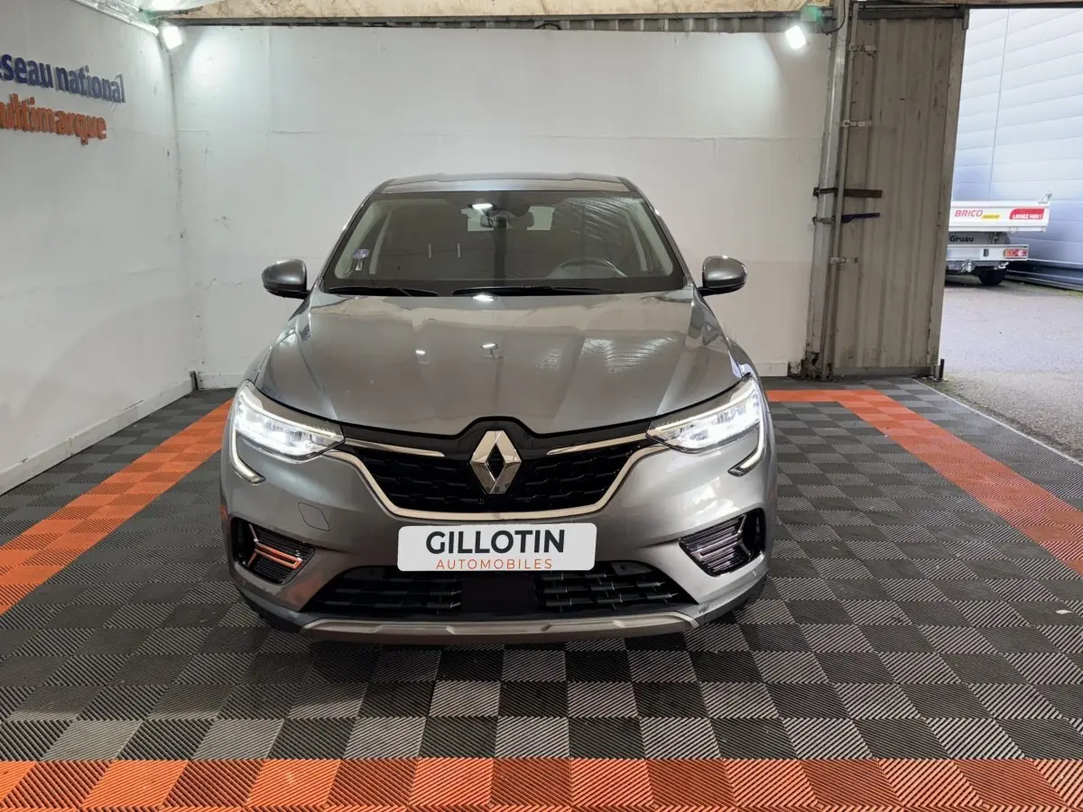 Vue avant d’un Renault Arkana Business E-TECH 145 gris foncé avec phares LED allumés dans un garage.