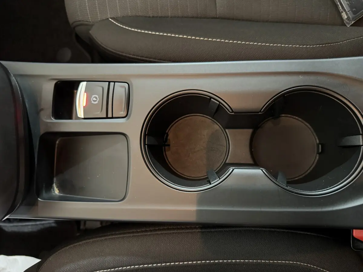 Vue rapprochée de la console centrale noire avec porte-gobelets et bouton frein à main électrique allumé sur Renault Arkana Business E-TECH 2022.