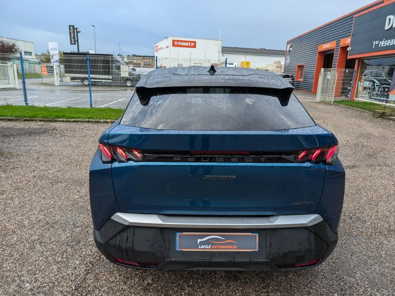 Vue arrière d’un Peugeot 3008 GT hybride bleu métallisé avec feux arrière à griffes LED et bandeau noir laqué.