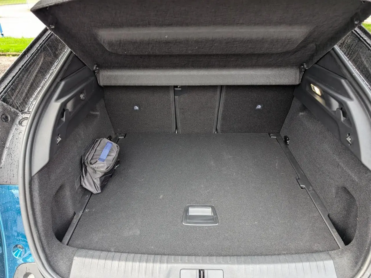 Coffre ouvert d’un Peugeot 3008 bleu métallisé, montrant un espace de chargement propre avec trousse noire sur le côté.