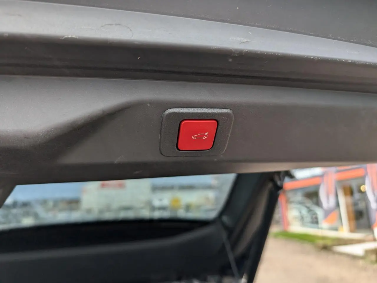 Bouton rouge d'ouverture électrique du hayon visible en gros plan sur un Peugeot 3008 bleu métallisé.