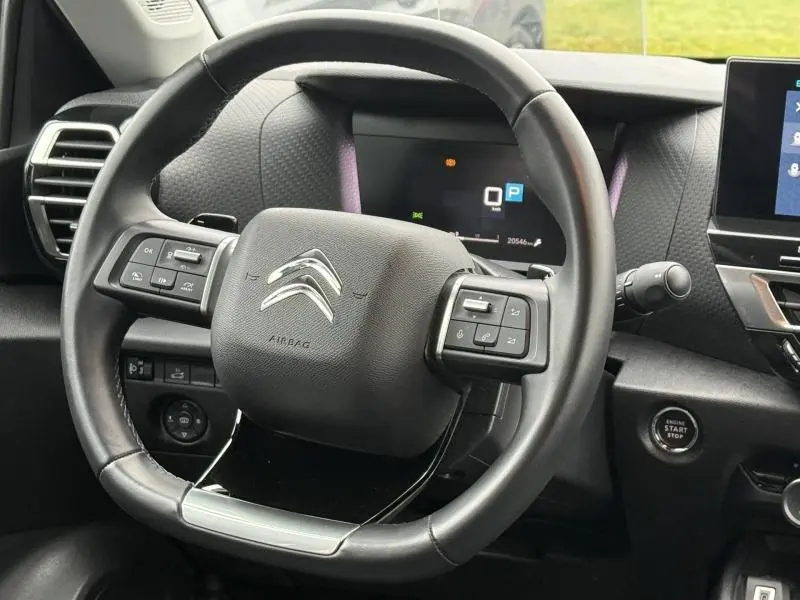 Vue rapprochée du volant noir du Citroën C4 X 2024 avec commandes intégrées et tableau de bord numérique en arrière-plan.