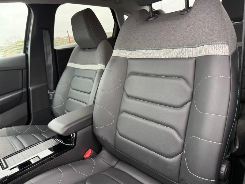 Gros plan sur les sièges avant en tissu et cuir noir du Citroën C4 X 2024, avec accoudoir central et surpiqûres contrastées.