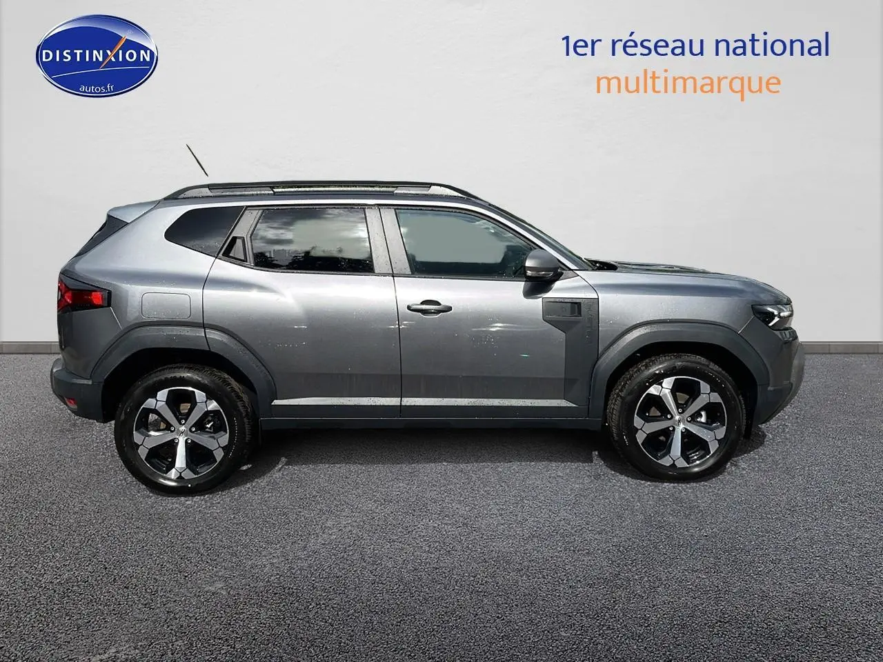 Profil côté droit du Dacia Duster 2025 gris schiste avec barres de toit et jantes alliage noires et argentées.
