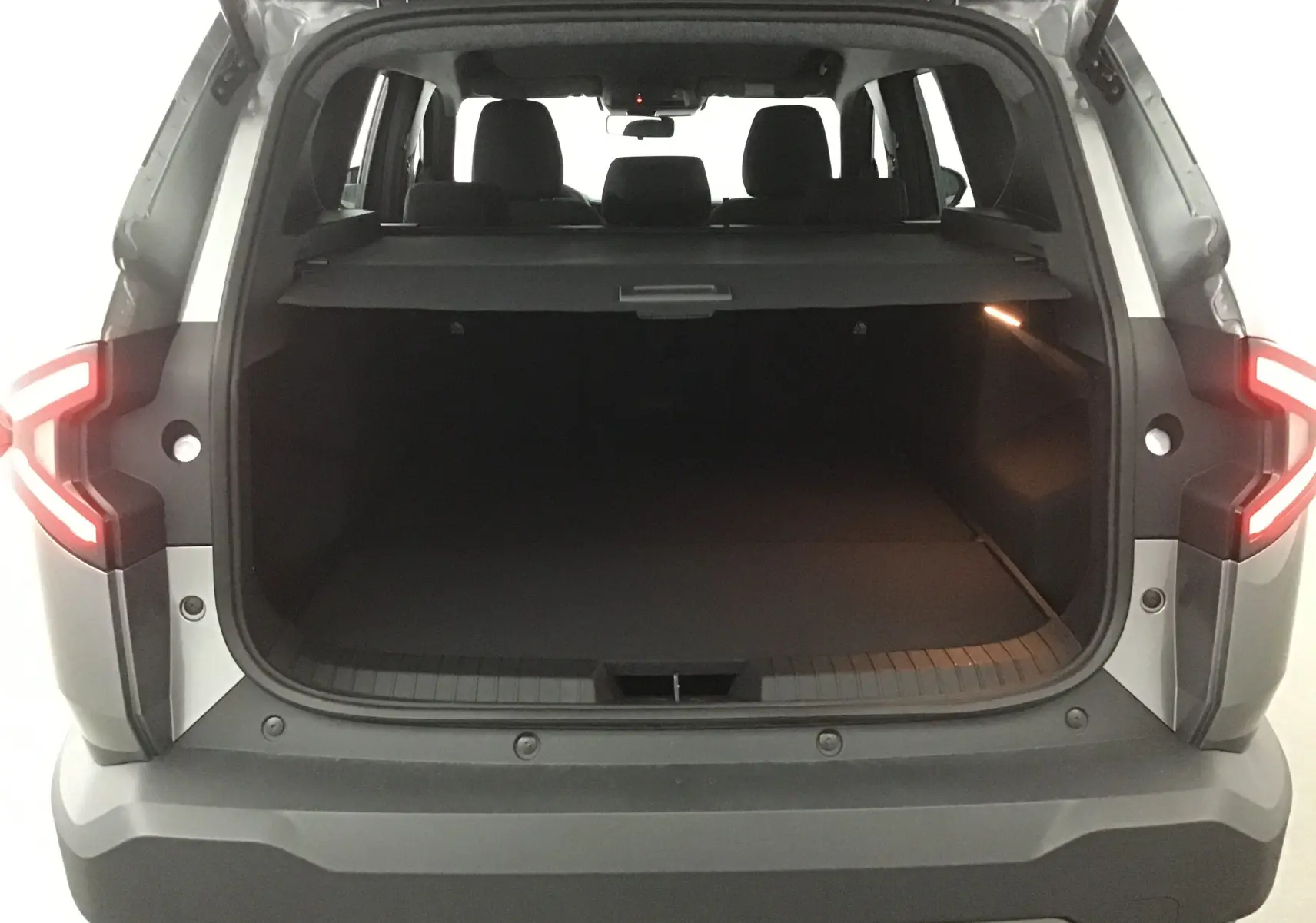 Coffre ouvert vu de l'arrière d'un Dacia Bigster gris schiste 2025 avec feux arrière allumés et intérieur spacieux.