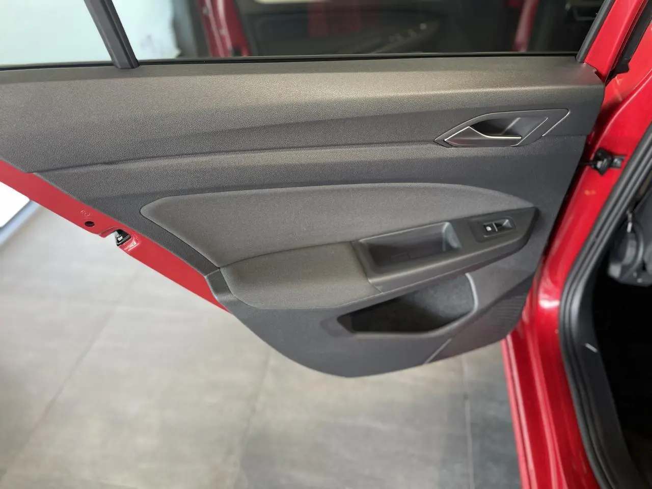 Porte arrière droite ouverte d'une Volkswagen Golf rouge métallisée, montrant le panneau intérieur gris foncé avec commande de vitre.