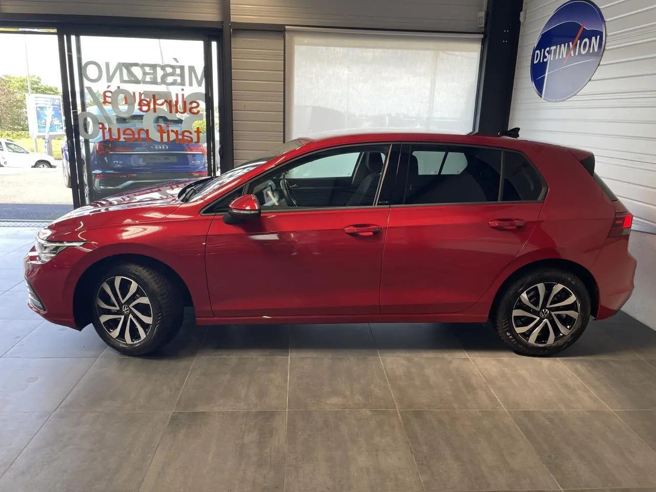 Profil droit d'une Volkswagen Golf rouge métal 2022 garée en intérieur avec jantes alliage distinctives.
