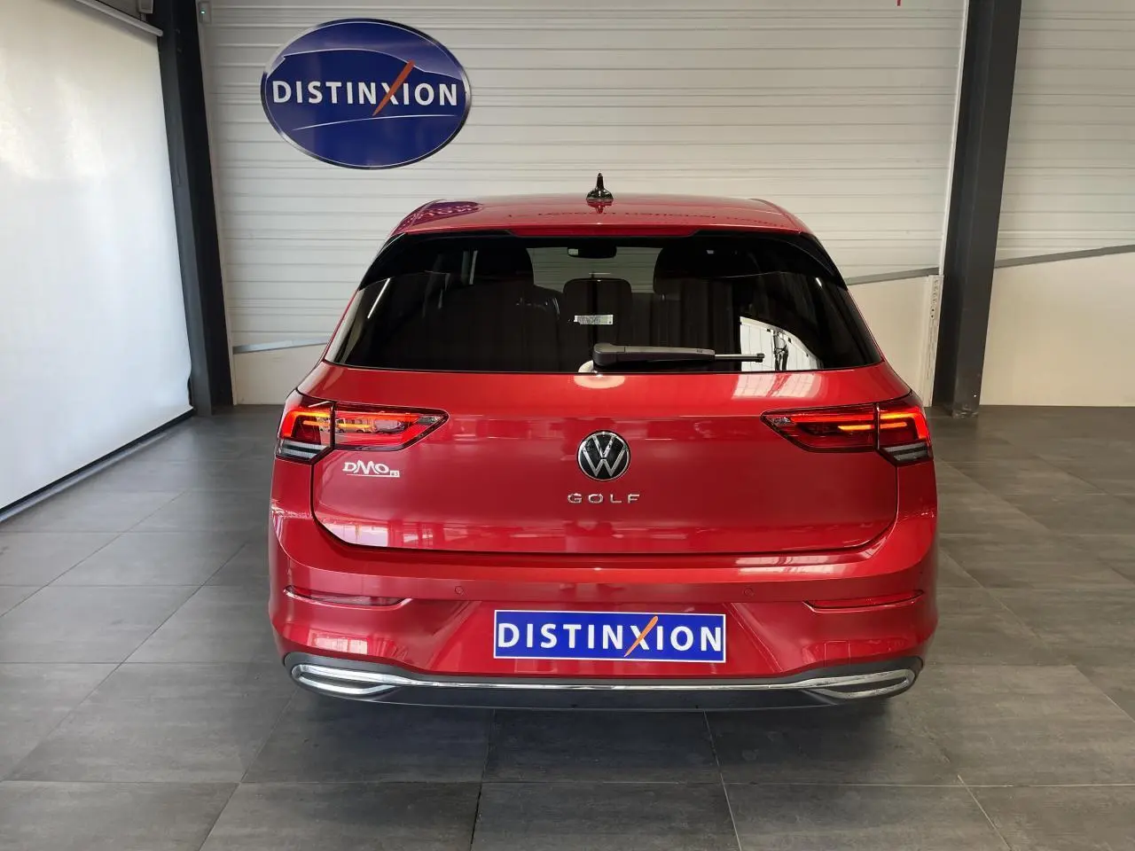 Vue arrière d'une Volkswagen Golf rouge métallisée 2022 avec feux LED et logo distinctif dans un showroom.