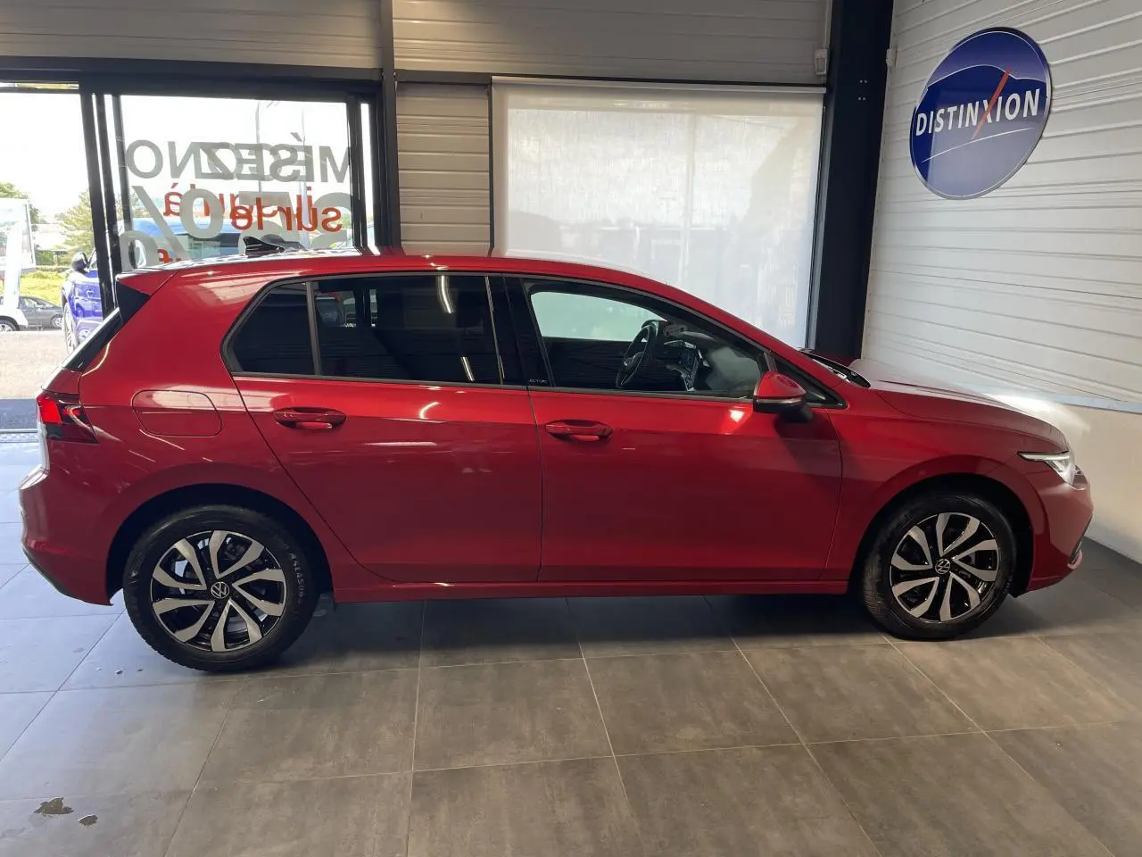 Profil côté gauche d'une Volkswagen Golf rouge métal 2022 avec jantes alliage et vitres teintées en showroom.