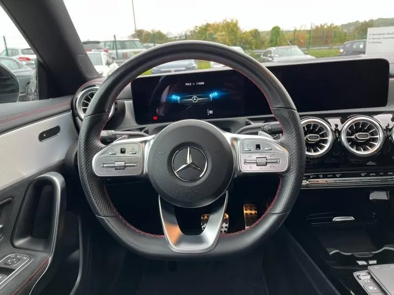 Vue rapprochée du volant cuir noir avec surpiqûres rouges et tableau de bord numérique de la Mercedes CLA Shooting Brake AMG Line.