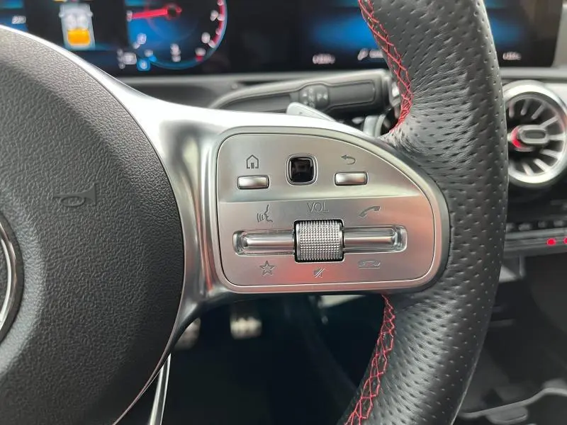 Gros plan sur les commandes argentées du volant sport en cuir noir avec surpiqûres rouges d'une Mercedes CLA Shooting Brake AMG Line.