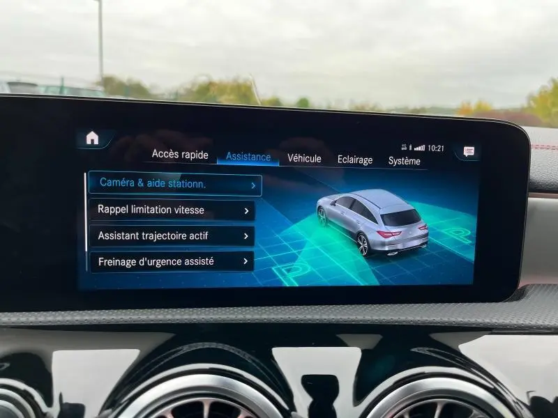 Écran tactile intérieur affichant l'assistance à la conduite avec vue 3/4 arrière d'une Mercedes CLA Shooting Brake gris montagne.