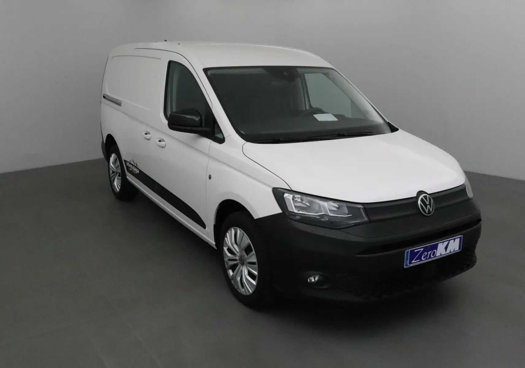 Vue 3/4 avant d'un Volkswagen Caddy Maxi blanc avec bouclier noir et logo Himalaya sur la porte côté droit.