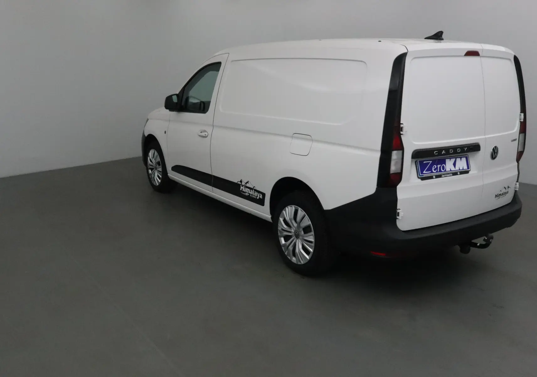 Vue 3/4 arrière droite d'un utilitaire Volkswagen Caddy Maxi blanc avec logo Himalaya et attelage visible.