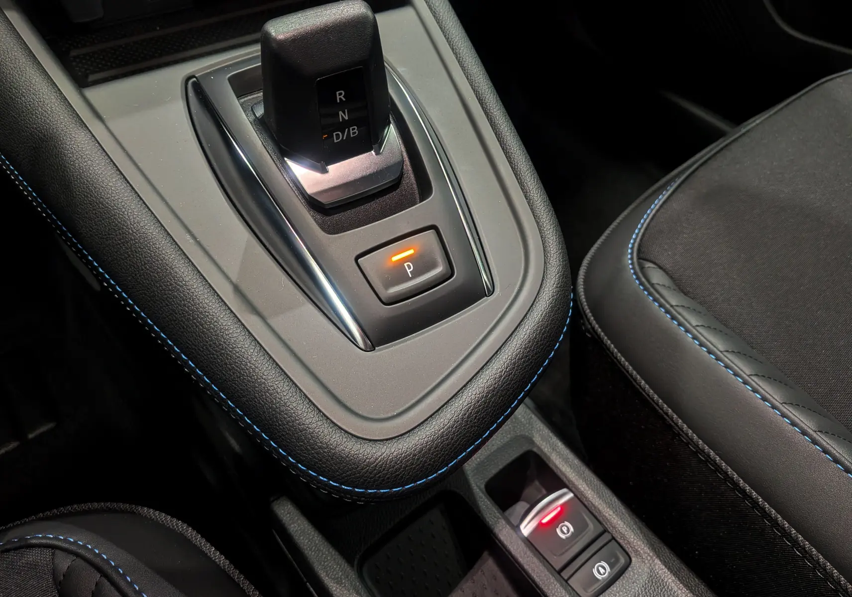 Gros plan sur la console centrale noire étoilé du Renault Captur E-TECH avec levier de vitesses et bouton de frein à main électrique.
