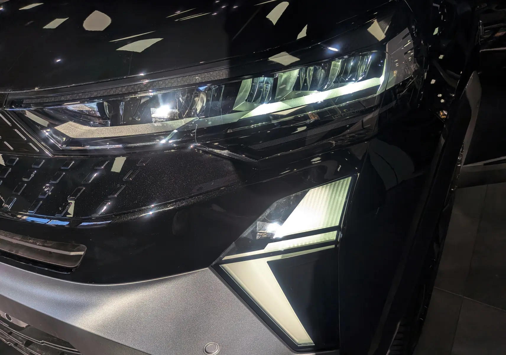 Gros plan sur le phare avant droit du Renault Captur E-TECH noir étoilé, soulignant ses feux LED modernes et détails anguleux.