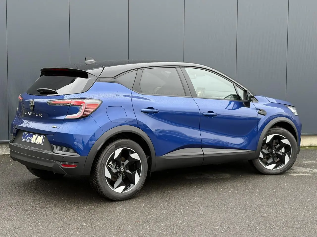 Vue 3/4 arrière droite du Renault Captur 2025 bleu Iron avec jantes aluminium noires et toit biton noir.