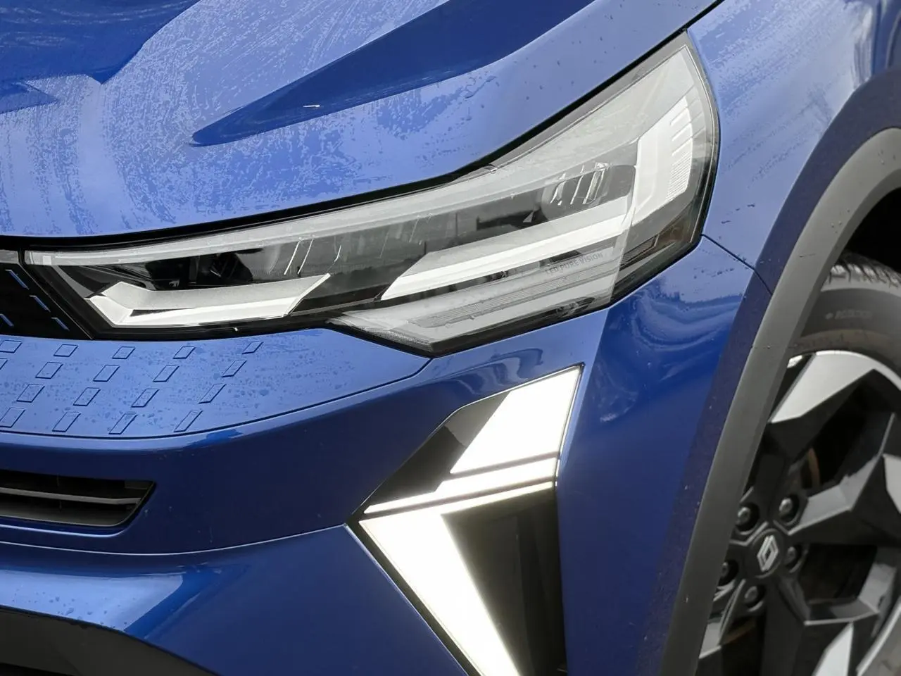 Gros plan sur l'avant droit du Renault Captur Bleu Iron, mettant en valeur les phares LED et la jante aluminium 18 pouces.