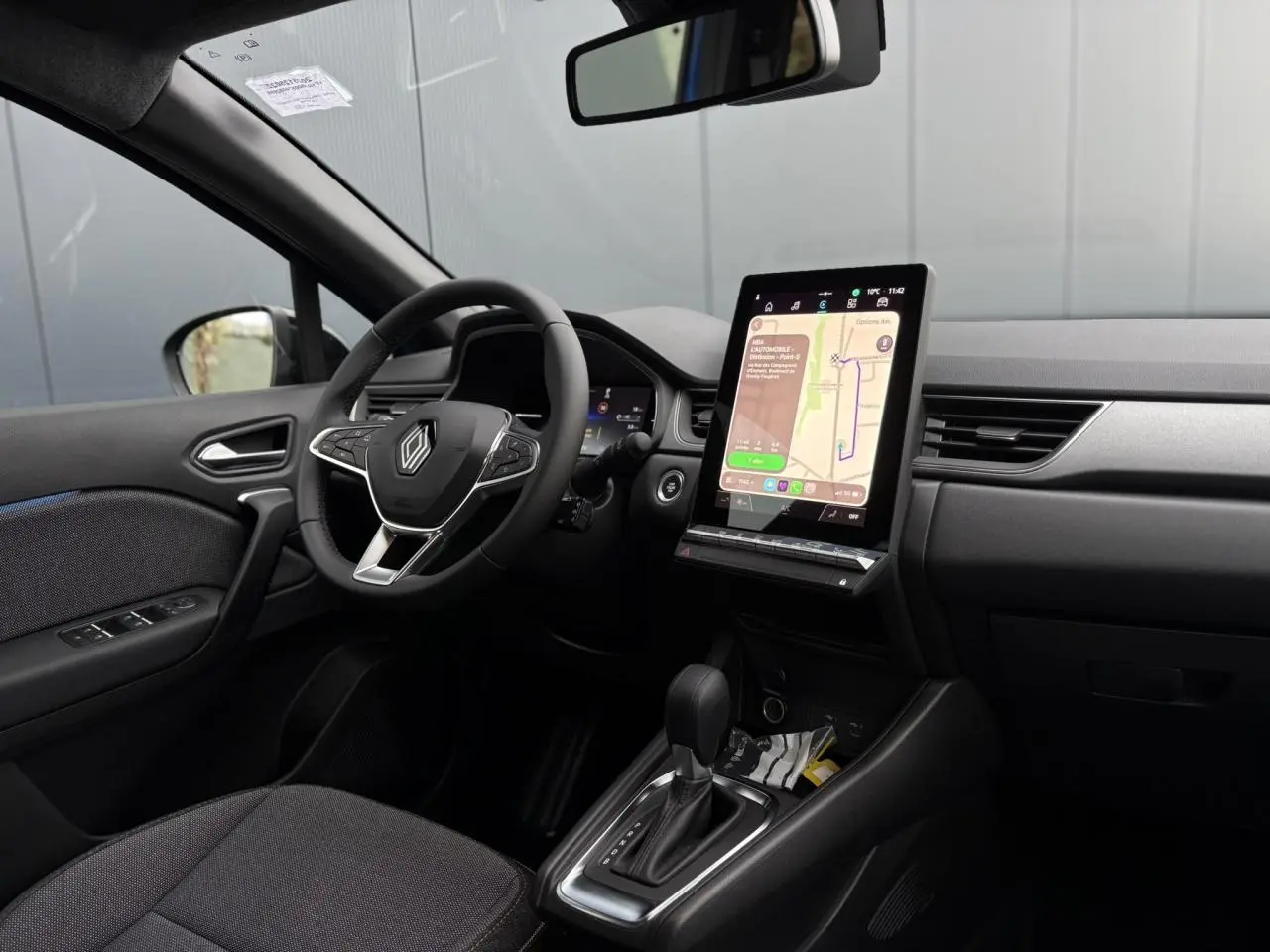Vue intérieure côté conducteur du Renault Captur bleu Iron 2025, avec écran tactile vertical et volant multifonction.