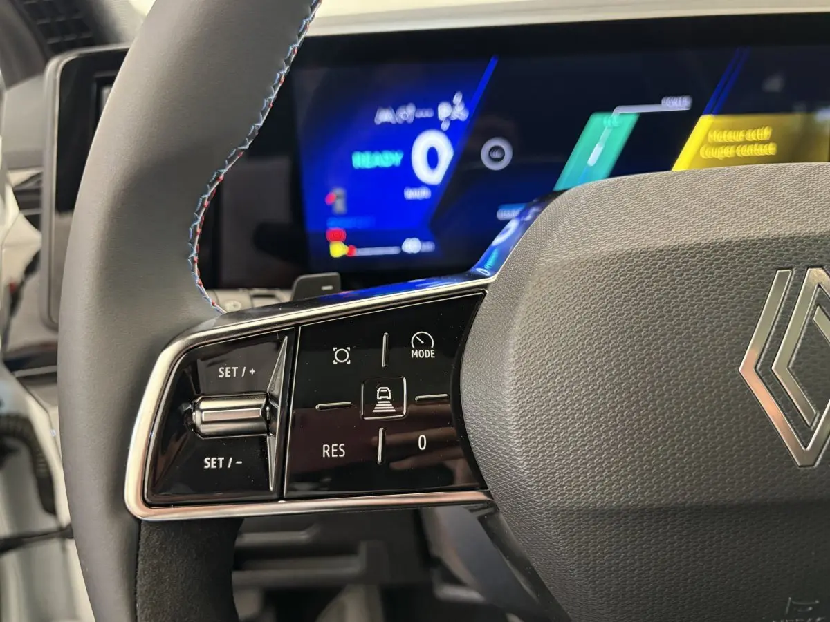 Gros plan sur le volant cuir et suède avec commandes multifonctions du Renault Espace blanc, tableau de bord numérique en arrière-plan.