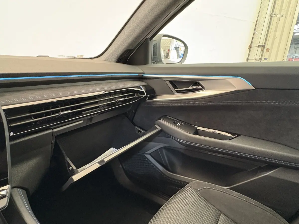 Vue intérieure côté passager du tableau de bord noir avec éclairage bleu et boîte à gants ouverte du Renault Espace 2025 esprit Alpine.