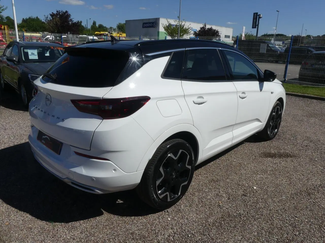 Opel Grandland blanc métallisé en vue 3/4 arrière droit avec toit noir brillant et jantes noires.