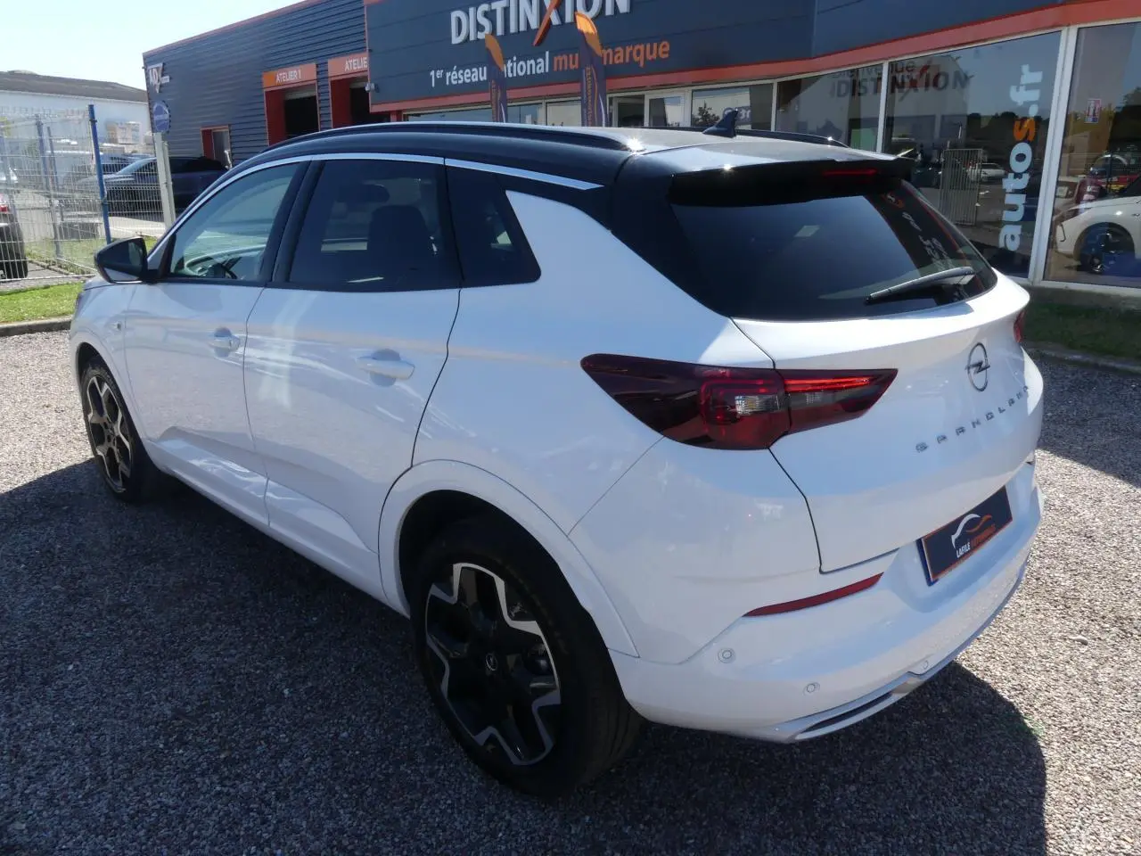 Opel Grandland blanc métallisé vu 3/4 arrière droit, toit noir brillant et jantes alliage noires distinctives.