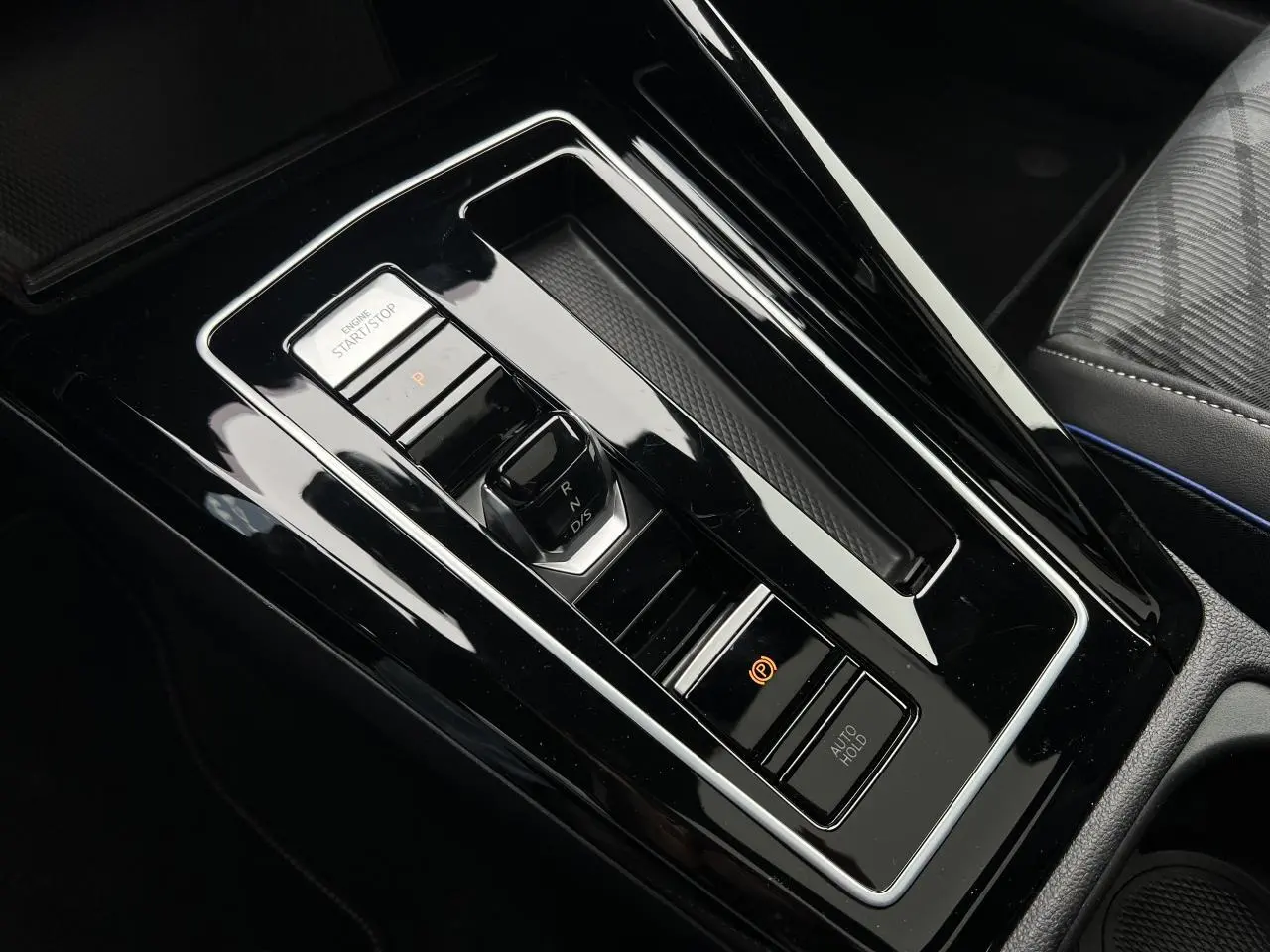 Vue rapprochée de la console centrale noire brillante de la Volkswagen Golf VIII R-Line avec sélecteur de boîte automatique et bouton start/stop.