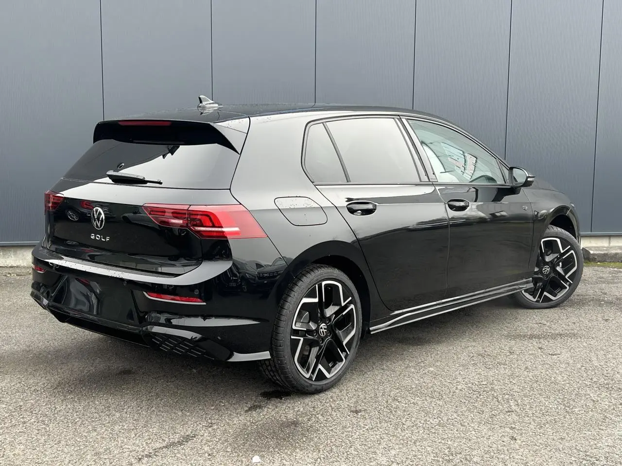 Vue 3/4 arrière droite d'une Volkswagen Golf VIII noire avec jantes alliage 18 pouces et toit ouvrant panoramique.