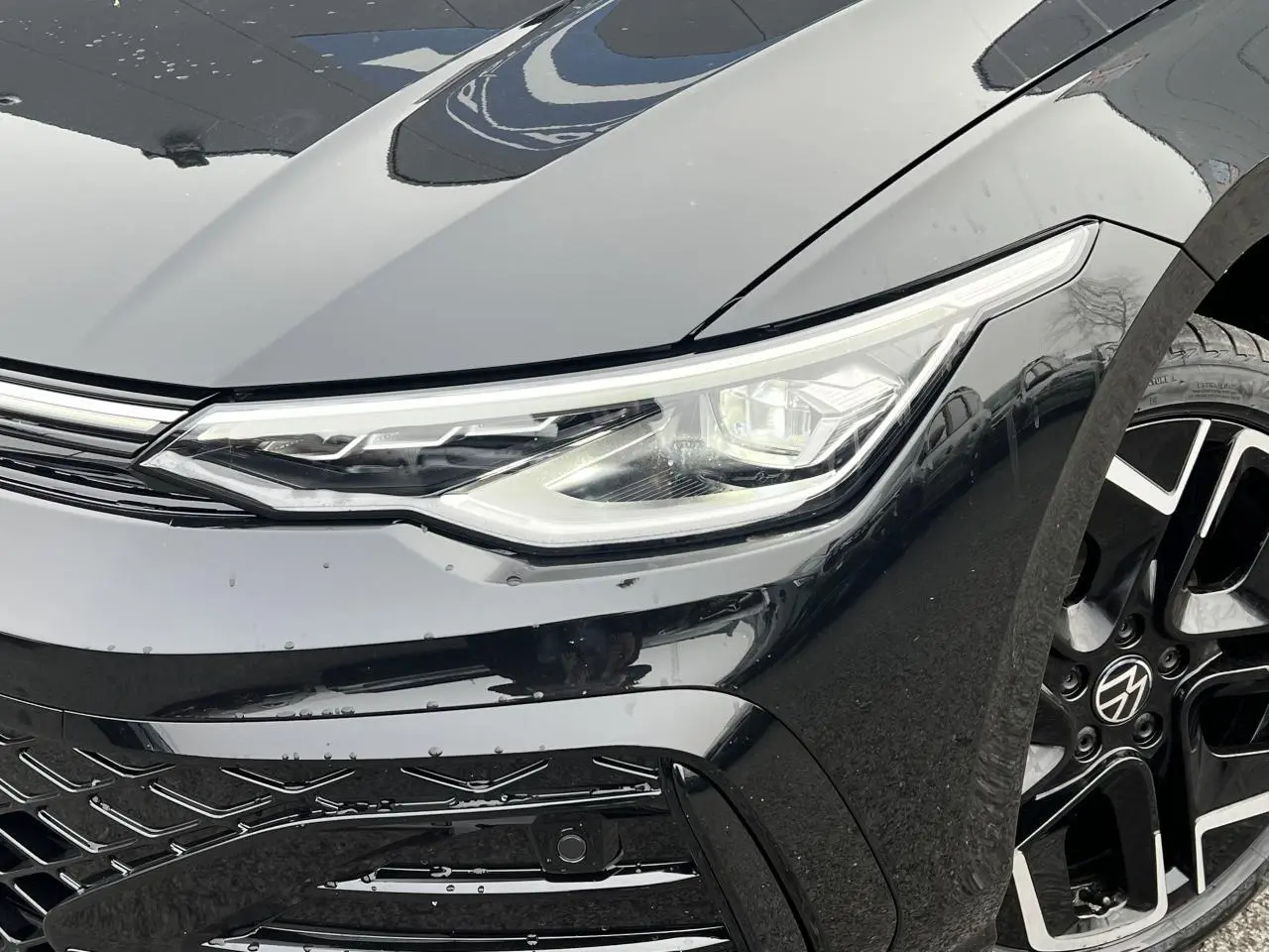Gros plan sur l'avant droit noir brillant d'une Volkswagen Golf VIII R-Line, mettant en valeur le phare LED et la jante alliage 18 pouces.