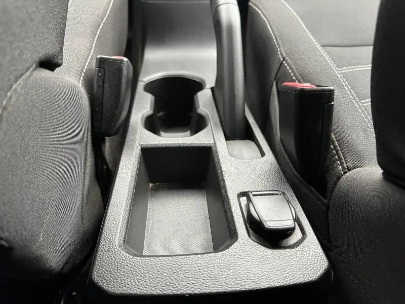 Gros plan sur la console centrale noire entre les sièges avant du Dacia Jogger 2025, avec porte-gobelet et frein à main.