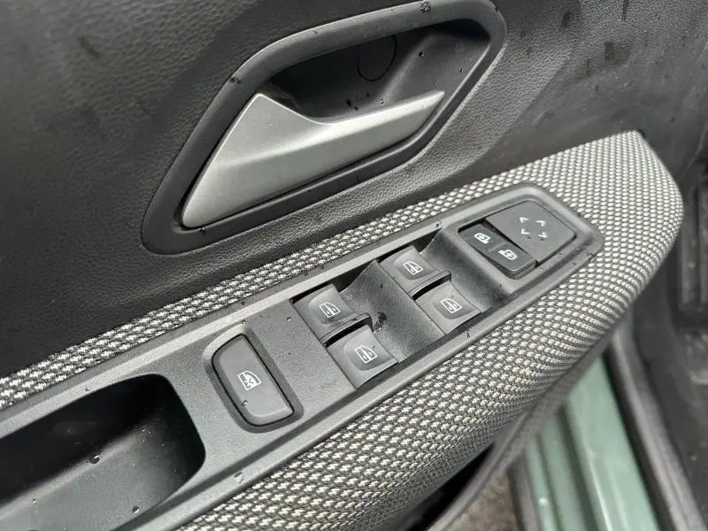 Gros plan sur la commande des vitres électriques côté conducteur du Dacia Jogger 2025, avec poignée argentée et tissu gris texturé.