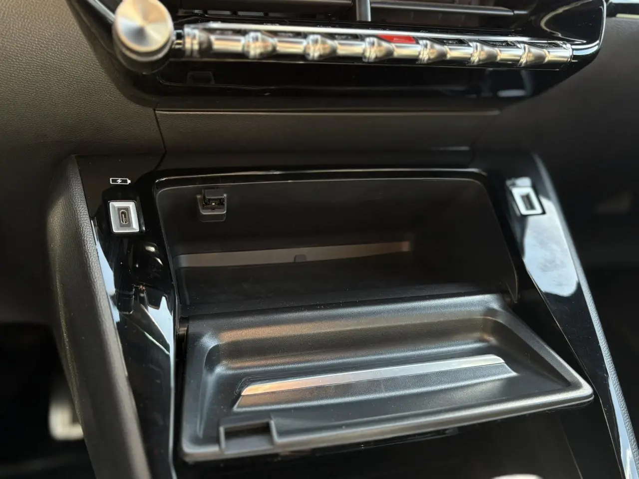 Gros plan sur la console centrale noire brillante du Peugeot 2008 GT 2021 avec prises USB et rangement ouvert.
