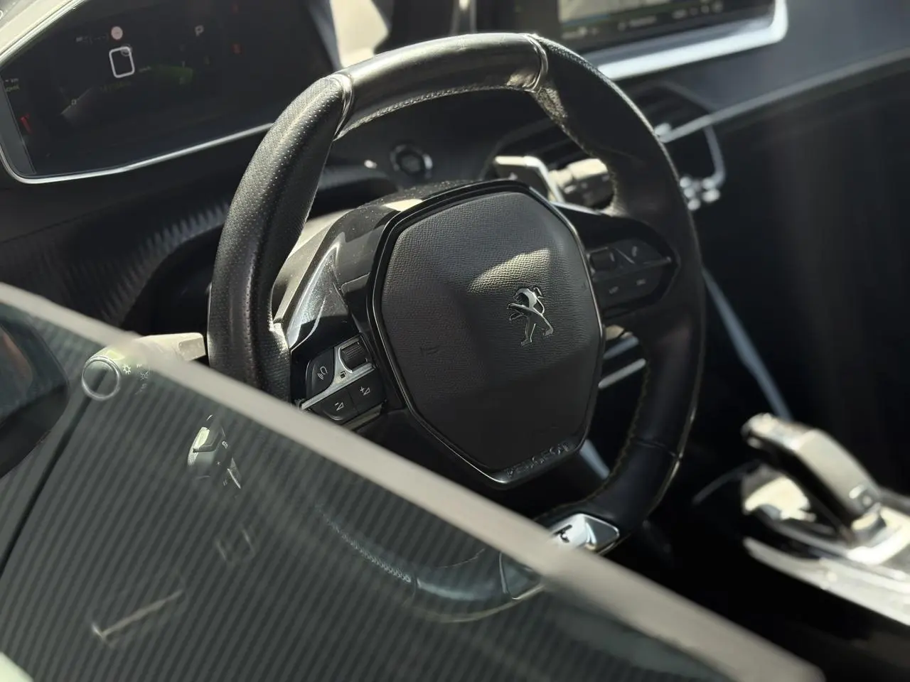 Vue rapprochée du volant cuir noir avec logo Peugeot du 2008 GT, montrant aussi la console centrale et levier de vitesse.