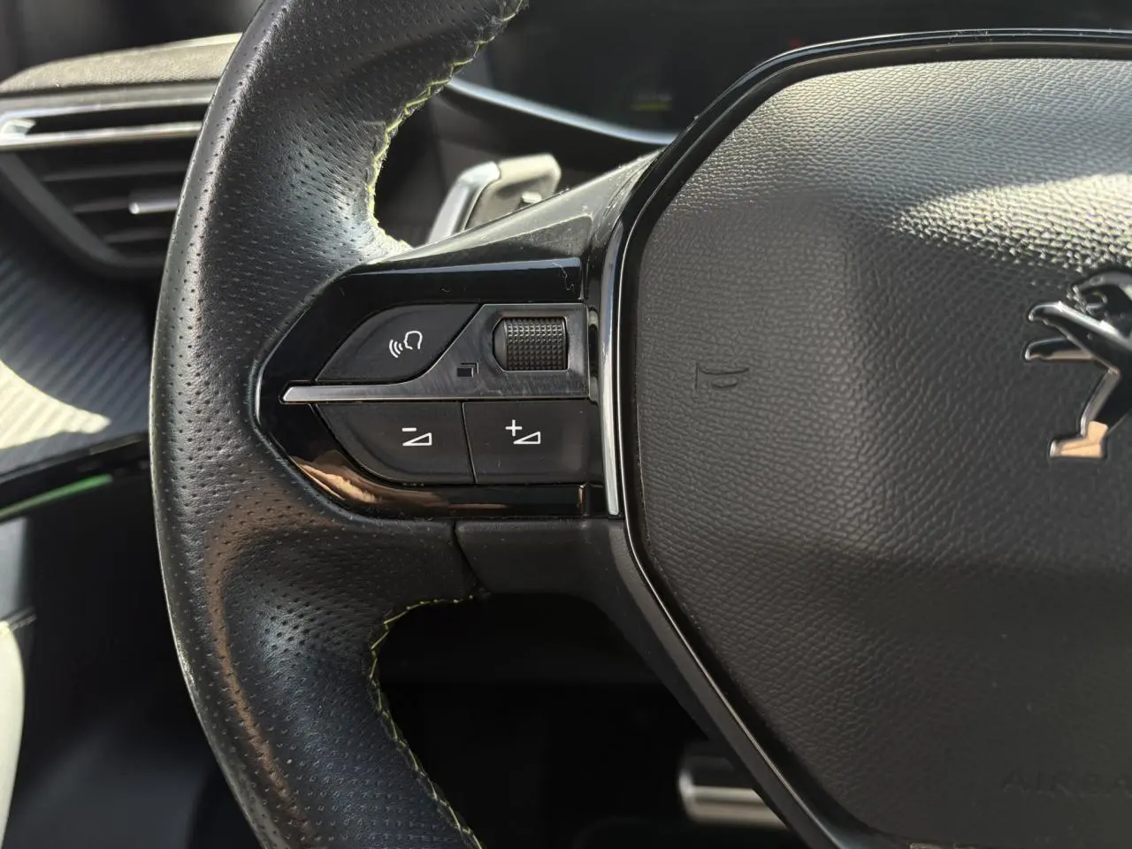 Gros plan sur le côté gauche du volant cuir noir du Peugeot 2008 GT avec surpiqûres vertes et commandes multimédia intégrées.