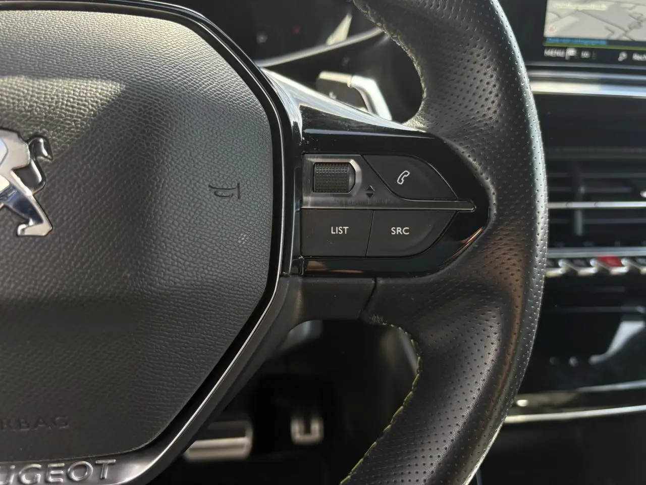 Gros plan sur le volant cuir perforé noir avec commandes multimédia et surpiqûres vertes du Peugeot 2008 GT 2021.
