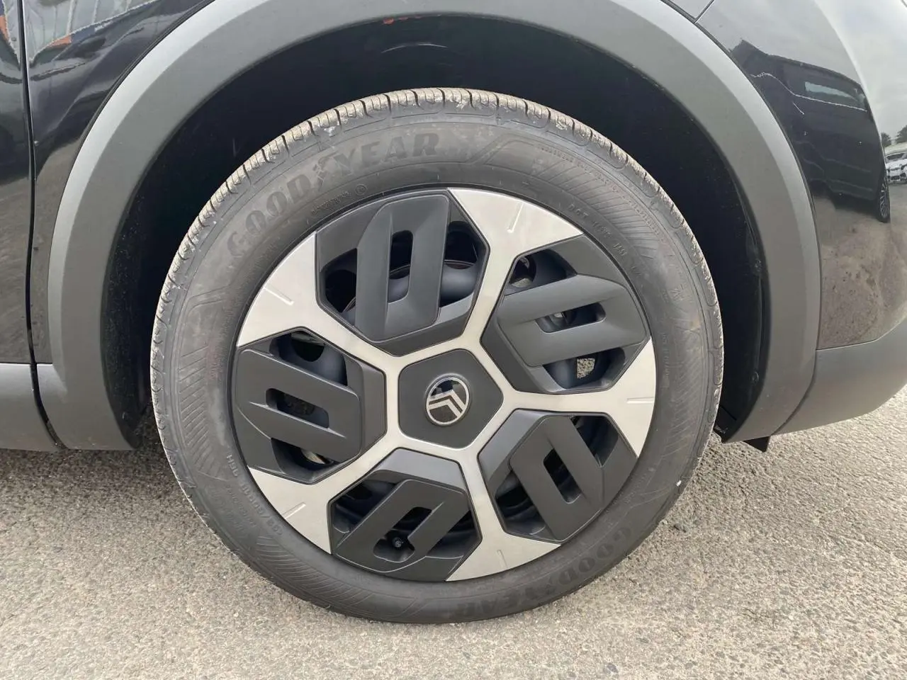 Gros plan sur la roue avant gauche noire Perla Nera d'une Citroën C4 hybride avec jante au design géométrique bicolore.