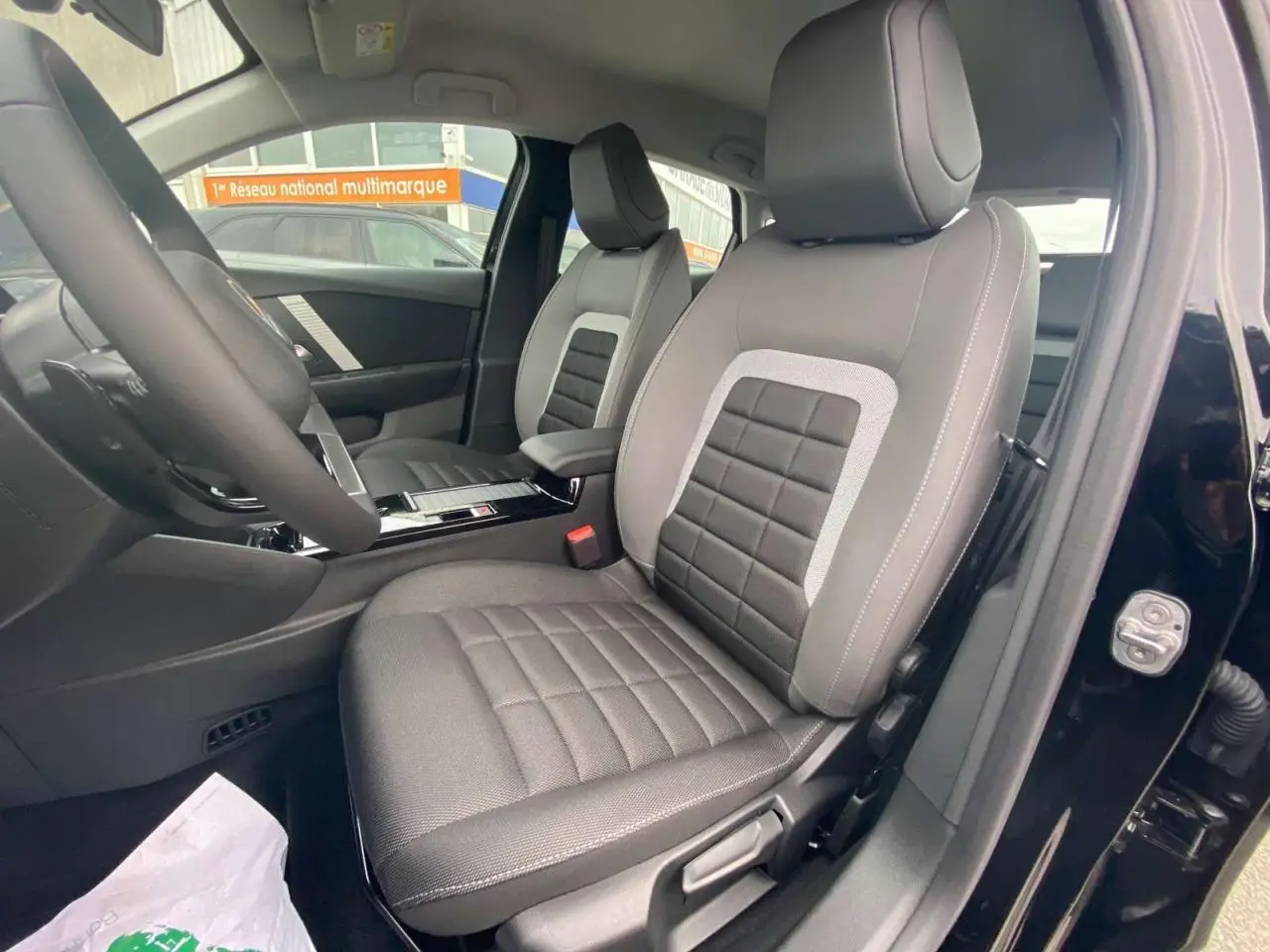 Intérieur de la Citroën C4 hybride 2025 vue côté conducteur, sièges gris avec surpiqûres blanches, porte noire ouverte.