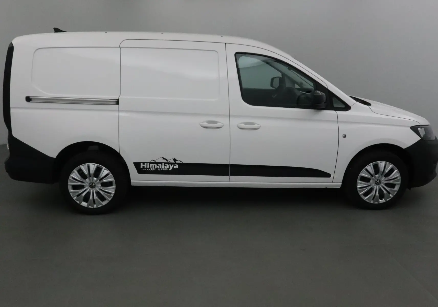 Profil droit d'un Volkswagen Caddy Maxi blanc avec logo Himalaya et jantes argentées, intérieur visible par la vitre.
