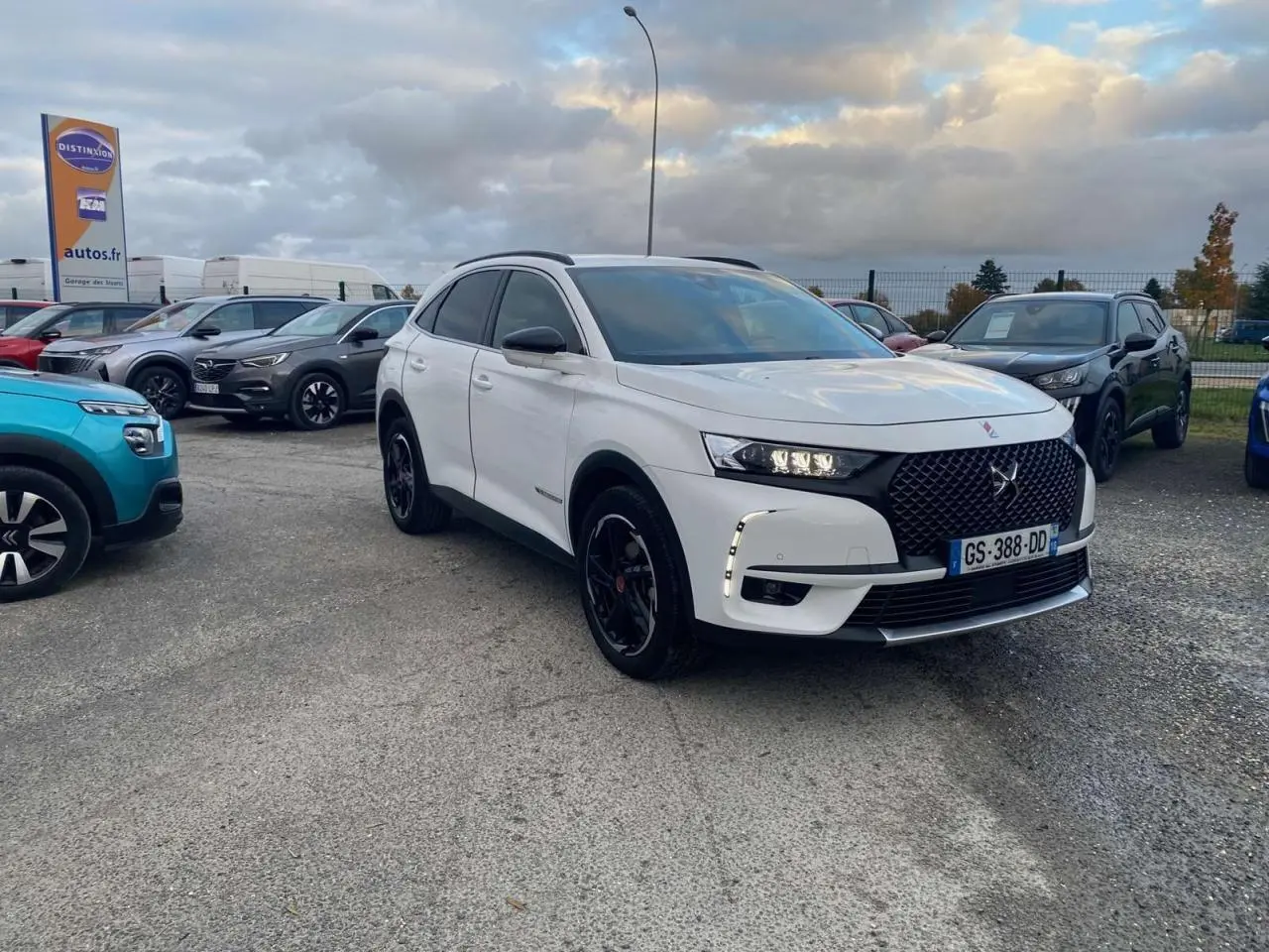 DS7 Crossback blanc en 3/4 avant droit avec calandre noire et jantes noires sur parking extérieur.