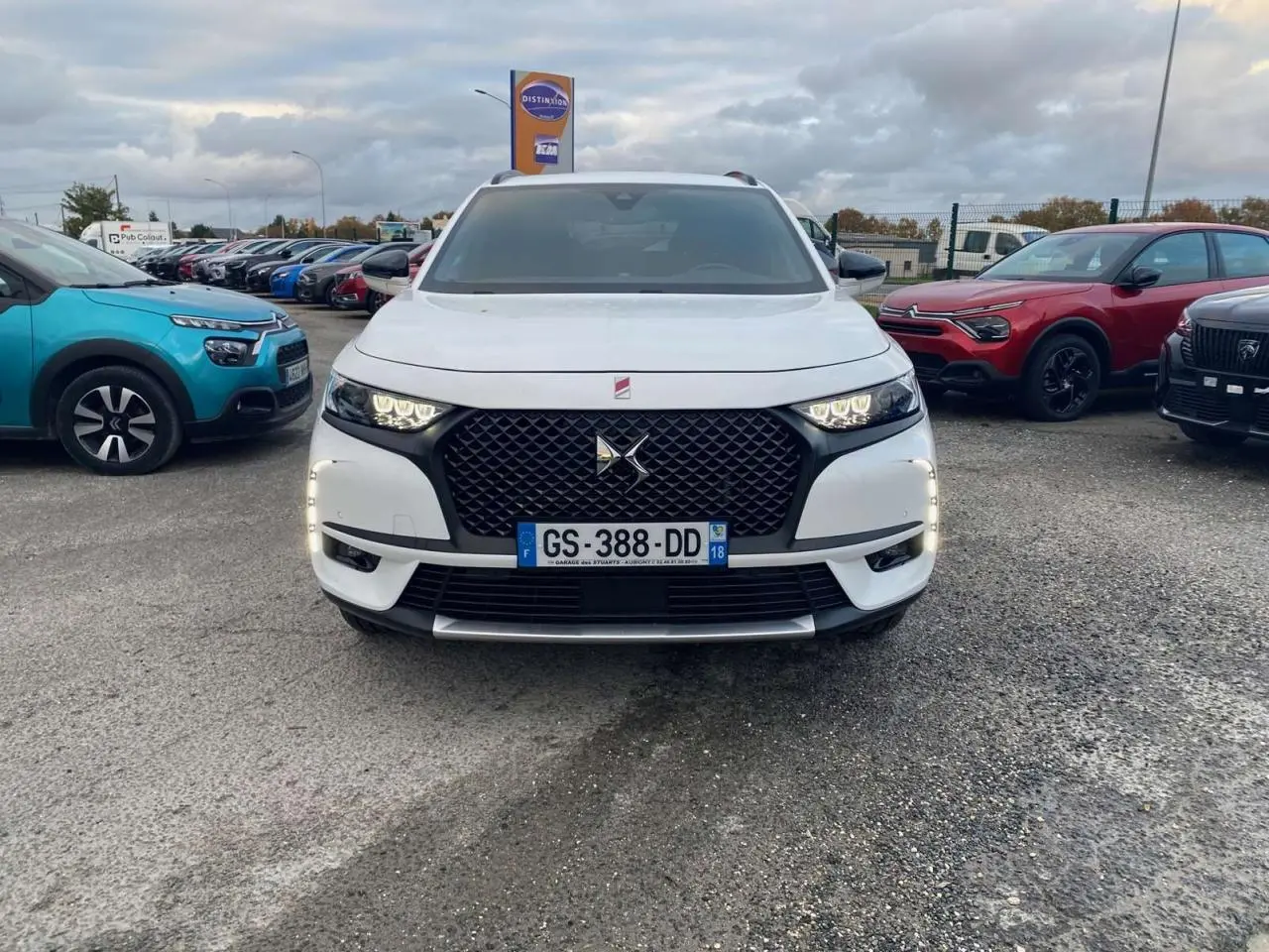 Vue frontale d'un DS7 Crossback blanc 2022 avec calandre noire et feux LED allumés sur un parking.