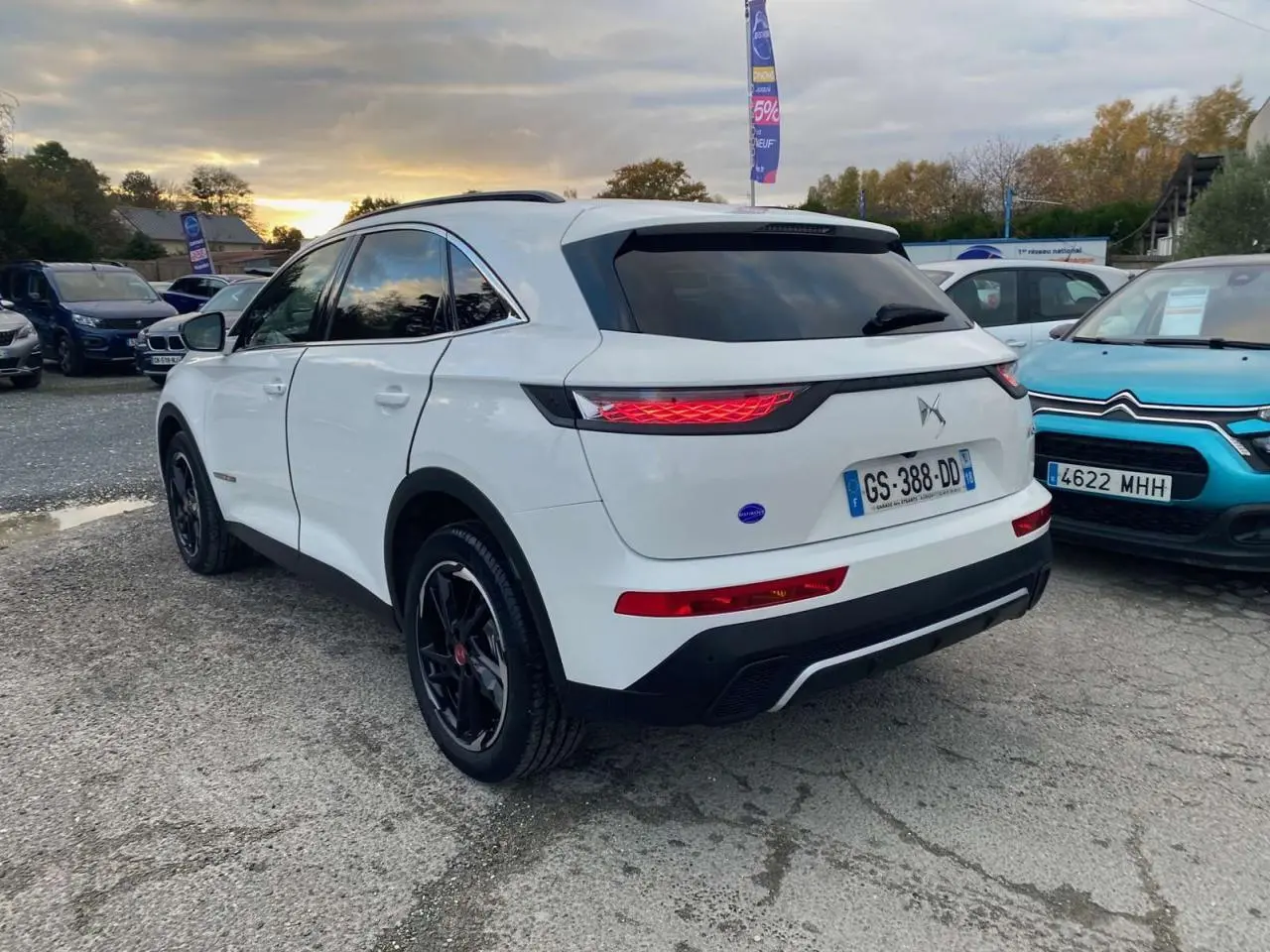 Vue 3/4 arrière droite d'un DS7 Crossback blanc 2022 avec jantes noires et feux arrière allumés.